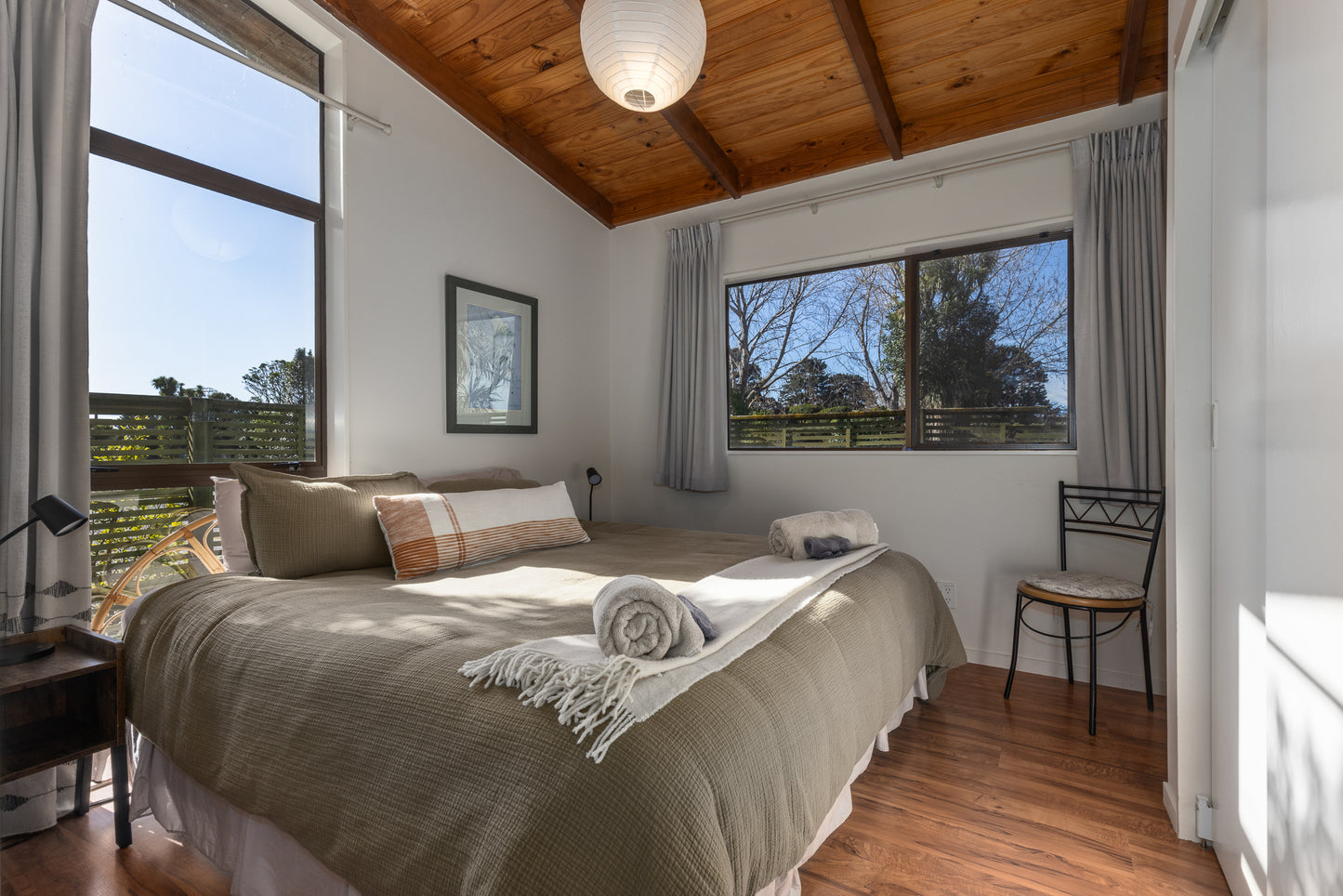 Bedroom with wooden ceiling, large windows, and a chair at Ngā Manu Nature Reserve